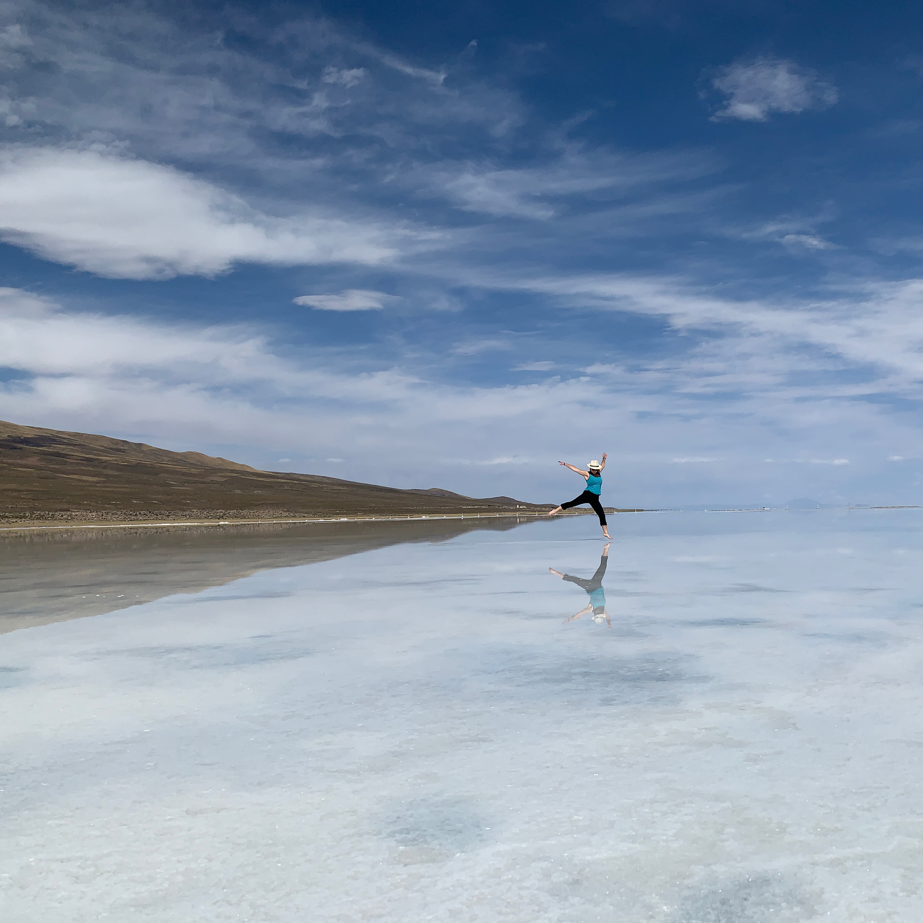 A distant figure leaps above still water reflecting the sky like a mirror.