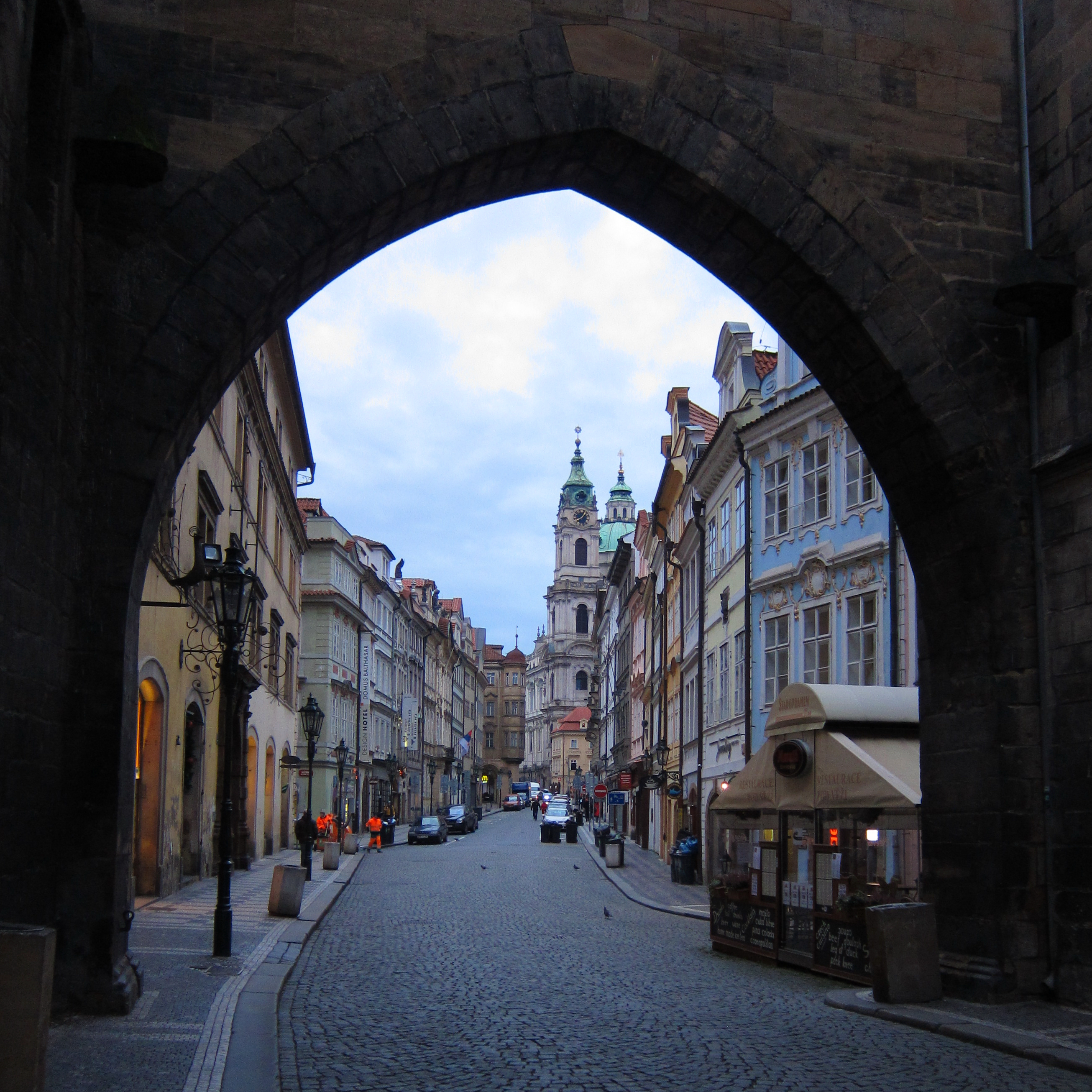 Pastel-painted old buildings crowded along cobbled street, seen through a pointed stone arch.